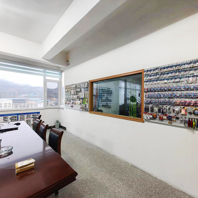 Office space with a large window overlooking mountains, featuring a wall display of various fishing rods, reels, and lures, emphasizing quality and selection.